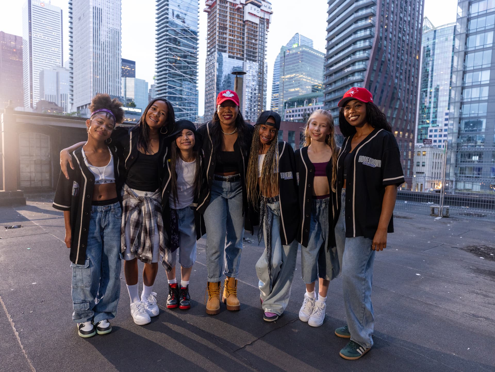 The Homegrown cast and artist together on a downtown Toronto rooftop at golden hour, wearing oversized black Homegrown baseball jerseys